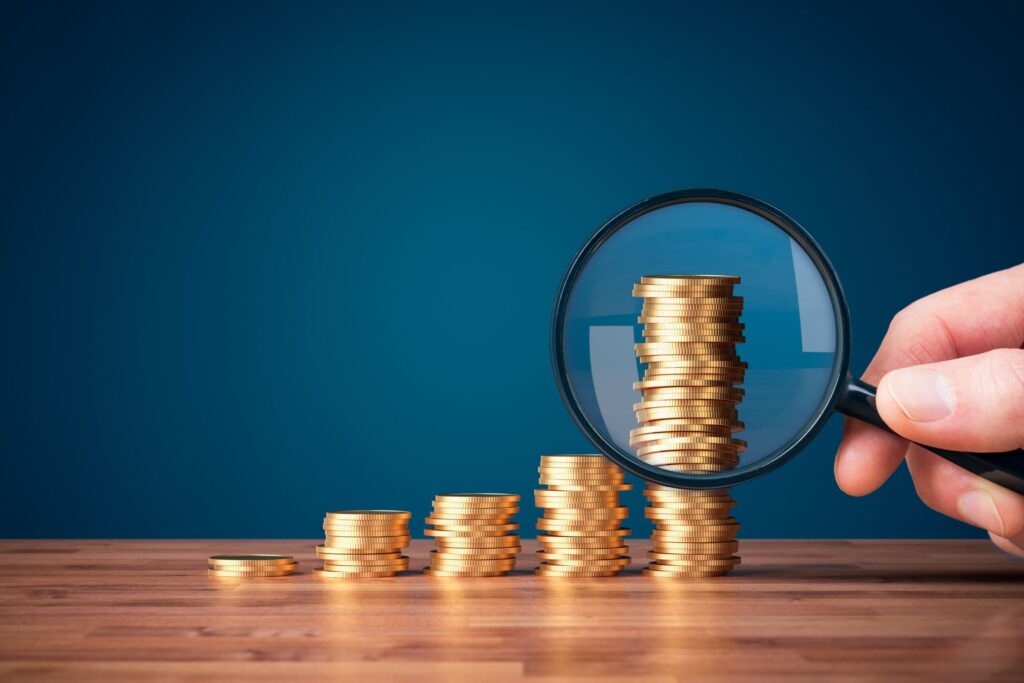 stacks of coins and a magnifying glass looking at it