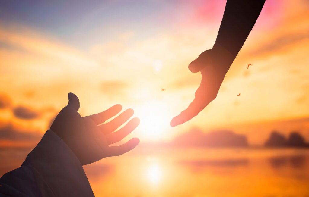 a hand reaching out for help with sun behind them